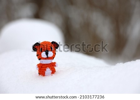 Knitted toy tiger on snow in a forest. Background for greeting card of celebration New Year 2022 of the tiger according to the Chinese calendar