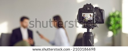 Blurry copy space banner background with a closeup shot of a modern video camera with a digital display recording an interview in a TV show studio. Mass media, television, and technology concepts