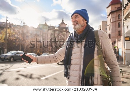 Grey haired mature man keeping his hand up while getting a taxi