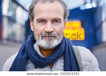 Male wearing scarf walking on street. He looking at the camera attentively