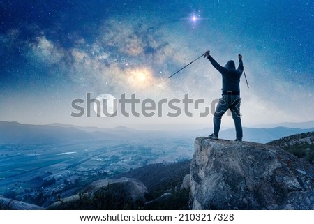 silhouette of a person on mountain top celebrating his achievement with hands up, Milky Way and Moon background	