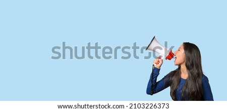Young woman yelling over a loud hailer or megaphone in a conceptual image on blue with copyspace Royalty-Free Stock Photo #2103226373