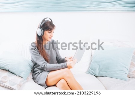 Brunette young woman listening to music with digital tablet and relaxing while sitting on sofa close up