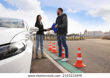 Young woman with instructor near car at driving school test track Royalty-Free Stock Photo #2103232898