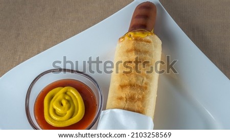 Appetizing French Hot Dog on white plate. Sausage in a bun with ketchup and mustard. Fast food concepts.