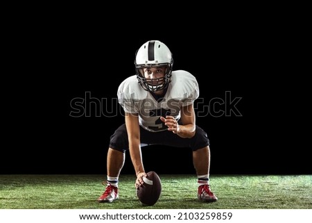Concentration. Portrait of American football player training isolated on dark studio background with green grass flooring. Concept of sport, movement, achievements. Copy space for ad Royalty-Free Stock Photo #2103259859