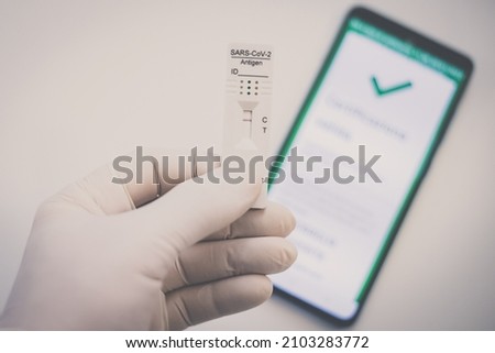 Closeup view of gloved hand with SARS-CoV-2 rapid antigen test nasal and phone with green digital certificate on display. Health, healthcare, corona virus, pandemic, illness, disease, travel concept