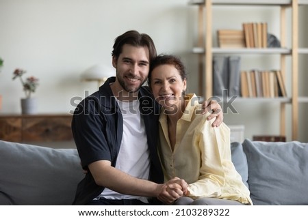 Portrait of affectionate young 30s handsome man cuddling happy loving middle aged old retired mother, relaxing together on comfortable couch, two generations bonding family relations concept.