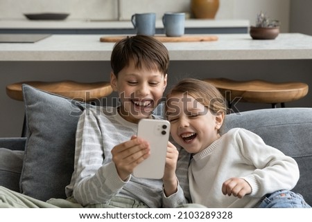 Happy cheerful gen Z sibling kids watching funny media on smartphone, making video call to parent, playing online game, virtual videogame, using learning app on internet, laughing. Parental control Royalty-Free Stock Photo #2103289328