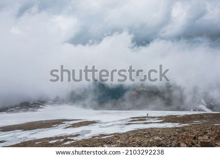 Dramatic landscape with people inside cloud above motley mountain valley. Tourists in cloud above multicolor valley. Low cloud on stone hill with snow. Awesome high mountain scenery in low clouds.