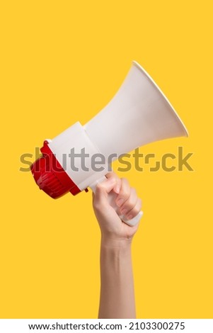Megaphone in woman hands on a yellow background.  Copy space.  Royalty-Free Stock Photo #2103300275