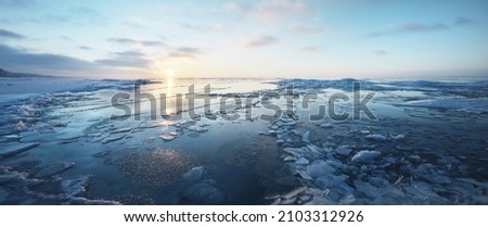 Panoramic view of the snow-covered shore of the frozen Baltic sea at sunset. Ice fragments close-up. Colorful cloudscape, soft sunlight. Symmetry reflections on the water. Christmas, seasons, winter Royalty-Free Stock Photo #2103312926