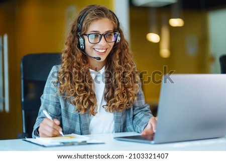 Call center agent with headset working on support hotline in modern office. Video conference.  Оnline training. Royalty-Free Stock Photo #2103321407