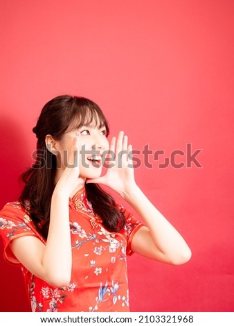 Cute asian girl wear a red chinese traditional cheongsam is shouting and holding her hands near her mouth with copyspace for the celebration of the Chinese New Year.