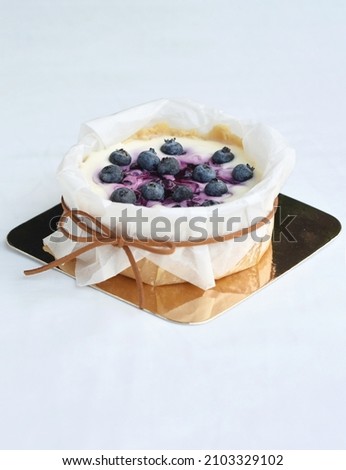 Blueberry Cheesecake on gold paper tray, wrapped with white paper and tied in a bow with brown string, On white background. Selective focus at blueberries on center of cake. For Pastry concept