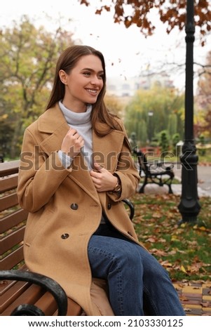 Beautiful young woman wearing stylish clothes on bench in autumn park