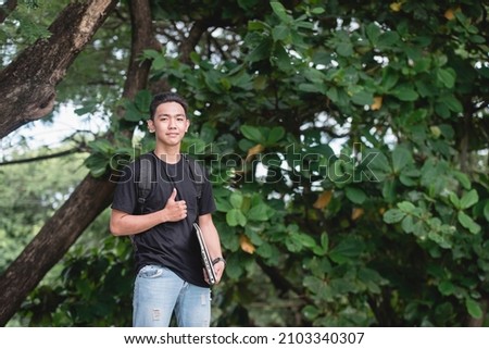 A young college student with a backpack and carrying his laptop while outside the school campus. Royalty-Free Stock Photo #2103340307
