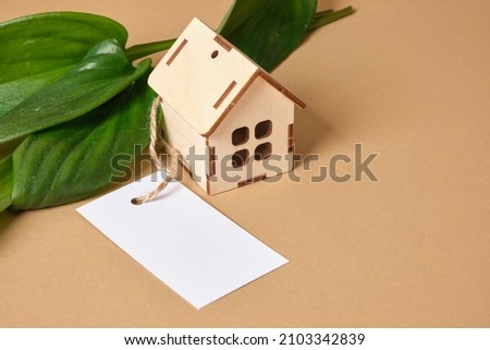 green leaves, miniature wooden house model and blank mock up white tag on brown background, eco house concept