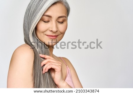 Portrait of gorgeous happy middle aged mature cheerful asian woman, senior older 50s lady pampering her hair eyes closed isolated on white. Ads of lifting anti wrinkle skin hair care spa. Copy space. Royalty-Free Stock Photo #2103343874