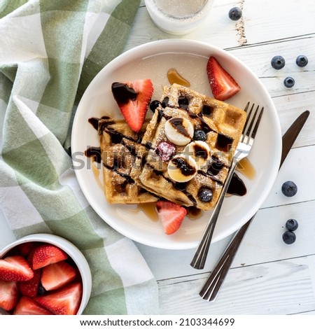 Top down view of waffles topped with fresh fruit, chocolate sauce and sugar.