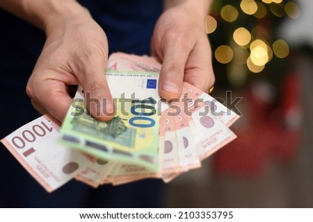 Man hand holding 100 euros with pile of Serbian dinar paper currency, 1000 dinars behind Royalty-Free Stock Photo #2103353795