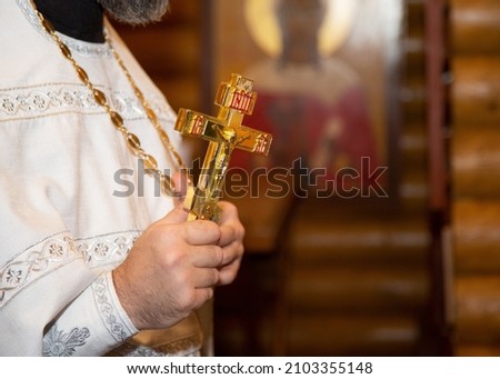 The priest of the Orthodox Church holds a golden cross. A golden cross in the hands of a priest. A male priest holds a large Orthodox cross. Royalty-Free Stock Photo #2103355148