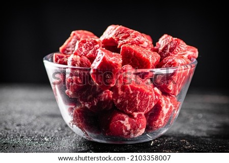 Raw pieces of beef in a glass bowl. On a black background. High quality photo