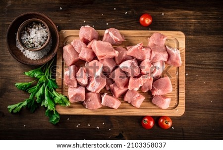 Pieces of raw pork on a cutting board with parsley and tomatoes. On a wooden background. High quality photo