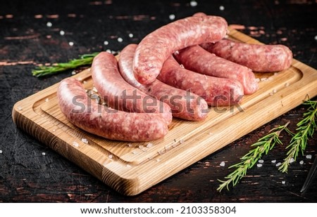 Raw sausages on a cutting board with a sprig of rosemary. On a rustic dark background. High quality photo
