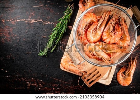 Boiled shrimp in a colander with a sprig of rosemary. Against a dark background. High quality photo