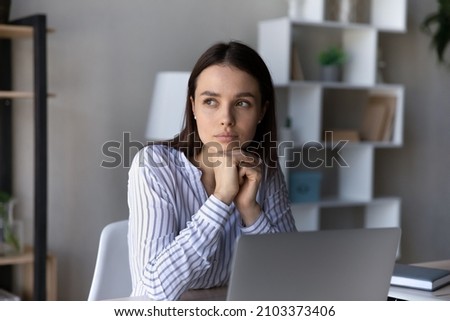 Serious thoughtful employee sitting at table with laptop, looking at window away, thinking over business problems, project, future career vision, feeling doubts, uncertain, dreaming and pondering Royalty-Free Stock Photo #2103373406