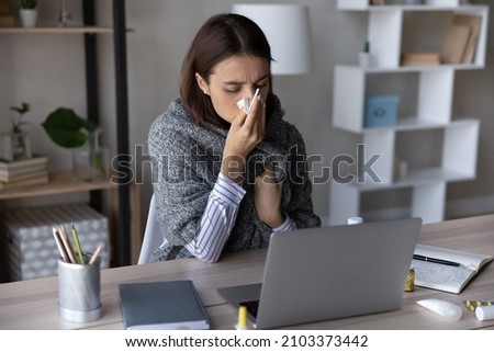 Frustrated sick girl wrapped in scarf suffering from cold, fever, flu, influenza. Ill woman feeling bad, unwell, blowing nose, holding tissue at face. Patient consulting doctor online on video call Royalty-Free Stock Photo #2103373442