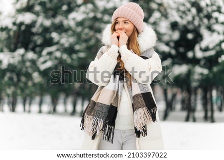 Portrait of a winter woman in warm clothes, Woman breathes on her arms to keep them warm on a cold winter day, Beautiful young woman outdoors. Cold weather concept, frozen hands Royalty-Free Stock Photo #2103397022