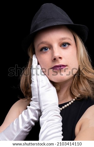 Beautiful young blond woman with blue eyes modeling with hats. Interior portrait with black background. Hats and closthes are vintage