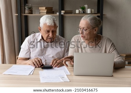Concentrated middle aged mature family couple calculating domestic expenditures or taxes, managing monthly budget, paying taxes or bills in computer e-banking application, planning investment. Royalty-Free Stock Photo #2103416675