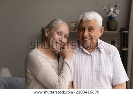 Portrait of smiling sincere affectionate older 60s beautiful hoary woman putting head on shoulder of happy loving elderly retired 80s husband, candid joyful mature family couple looking at camera.