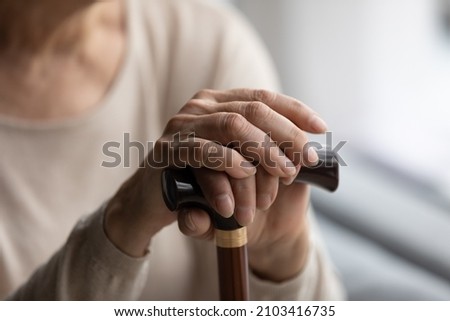 Close up focus on folded wrinkled female hands on wooden cane. Cropped thoughtful elderly senior grandmother having walking disability, using stick indoors, old retired people lifestyle concept. Royalty-Free Stock Photo #2103416735