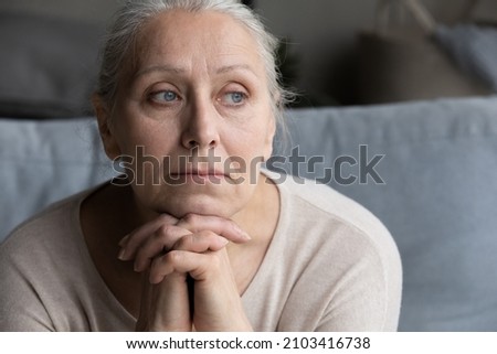 Head shot thoughtful old senior grandmother looking in distance, suffering from loneliness or psychological problems, recollecting bad memories, having nostalgic mood sitting on couch at home. Royalty-Free Stock Photo #2103416738