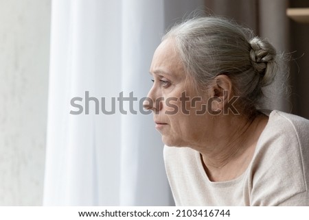 Side view head shot stressed unhappy middle aged mature hoary retired woman looking out of window in distance, thinking of health problems, suffering from loneliness or mourning at home, copy space. Royalty-Free Stock Photo #2103416744