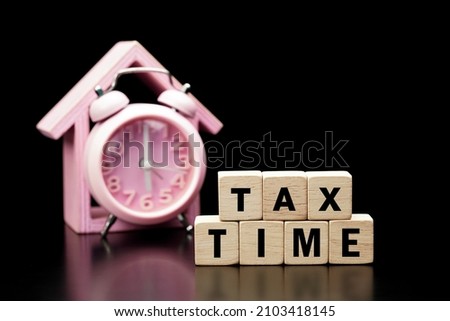Tax Concept. Tax time word is written on wood block and clock on black background. Tax time.