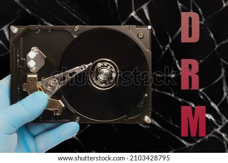 man in blue latex glove holds hard drive with abbreviation (drm) digital rights management on dark background, the concept of copyright protection