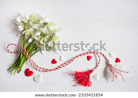 A bouquet of snowdrops flowers, red and white rope with tassels, hearts on a wooden background. Postcard for the holiday of March 1, space for text. Royalty-Free Stock Photo #2103431834