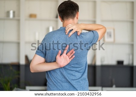 Pain between the shoulder blades, man suffering from backache at home, health problems concept Royalty-Free Stock Photo #2103432956