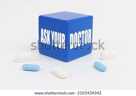 Medicine and health concept. On a white surface are pills and a blue cube that says - ASK YOUR DOCTOR