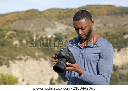 Concentrated man with black skin checking photos on dslr camera in nature