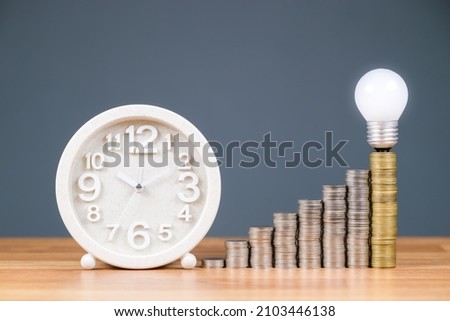 Time, money, and success : white clock with heap coins stairs and glowing light bulb on the top stage, savings and retirement plan, productivity, or investment concept Royalty-Free Stock Photo #2103446138