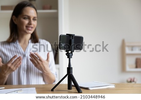 Positive trendy blogger woman speaking at smartphone webcam on tripod, recording post for vlog. Online teacher, coach working, giving webinar at home. Presenter taking video on cellphone. Close up