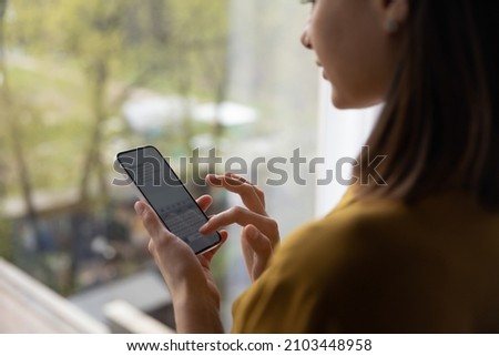 Woman chatting online on smartphone at window glass, typing text message, touching touchscreen keyboard, using messenger application. Millennial user holding mobile phone, close up, cropped shot Royalty-Free Stock Photo #2103448958