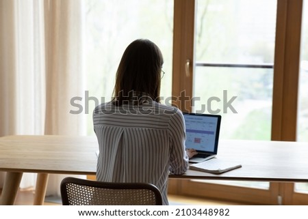 Back of young business woman working at home office workplace table, checking schedule, workday tasks on planner service on laptop screen. Female employee, student girl using online calendar app Royalty-Free Stock Photo #2103448982
