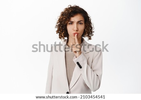 Angry businesswoman hushing, making shh shush taboo gesture, telling to keep quiet, standing in business suit over white background